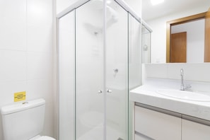 Une salle de bain moderne avec une douche à parois de verre, un lavabo blanc et un miroir au-dessus du lavabo.