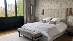 Ein Schlafzimmer mit einem großen Bett, einer Bank und Blick auf ein Gebäude durch das Fenster.