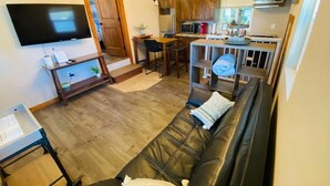 Ein Wohnzimmer mit einer schwarzen Ledersofa, einem flachbildfernseher an der Wand und einem Holzessttisch mit Stühlen.