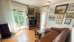 A living room with a brown leather sofa, wooden flooring, a television, and a dining table. - Holiday apartment with air conditioning (Jadranovo)