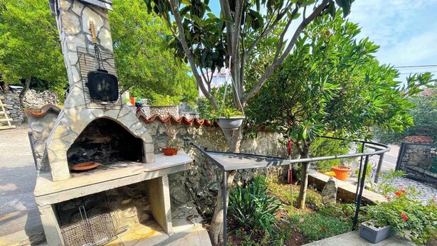 An outdoor stone-built pizza oven with a chimney, surrounded by potted plants and a stone wall. - Holiday apartment with air conditioning (Jadranovo)