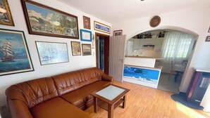 A living room with a brown leather sofa, a wooden coffee table, and various framed artworks on the walls. - Holiday apartment with air conditioning (Jadranovo)