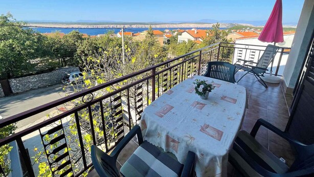 Een balkon met een tafel en stoelen, met uitzicht op de kust, huizen en een brug.