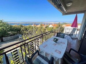 Un balcón con una mesa y sillas, con vistas a la costa, casas y un puente.