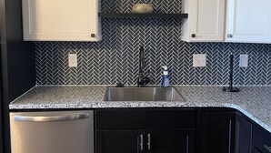 Een keuken met donkere kastjes, een granieten werkblad, een roestvrijstalen vaatwasser en een zwart-wit houten vlechtachterwand.