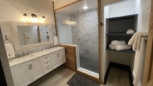 Een moderne badkamer met een grote spiegel, dubbele wastafels, een douchecabine en een handdoekrek.