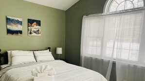 Ein ordentlich bezogenes Bett mit weißer Decke und Kissen, einer Nachttischlampe sowie zwei Wandbilder mit Naturmotiven.