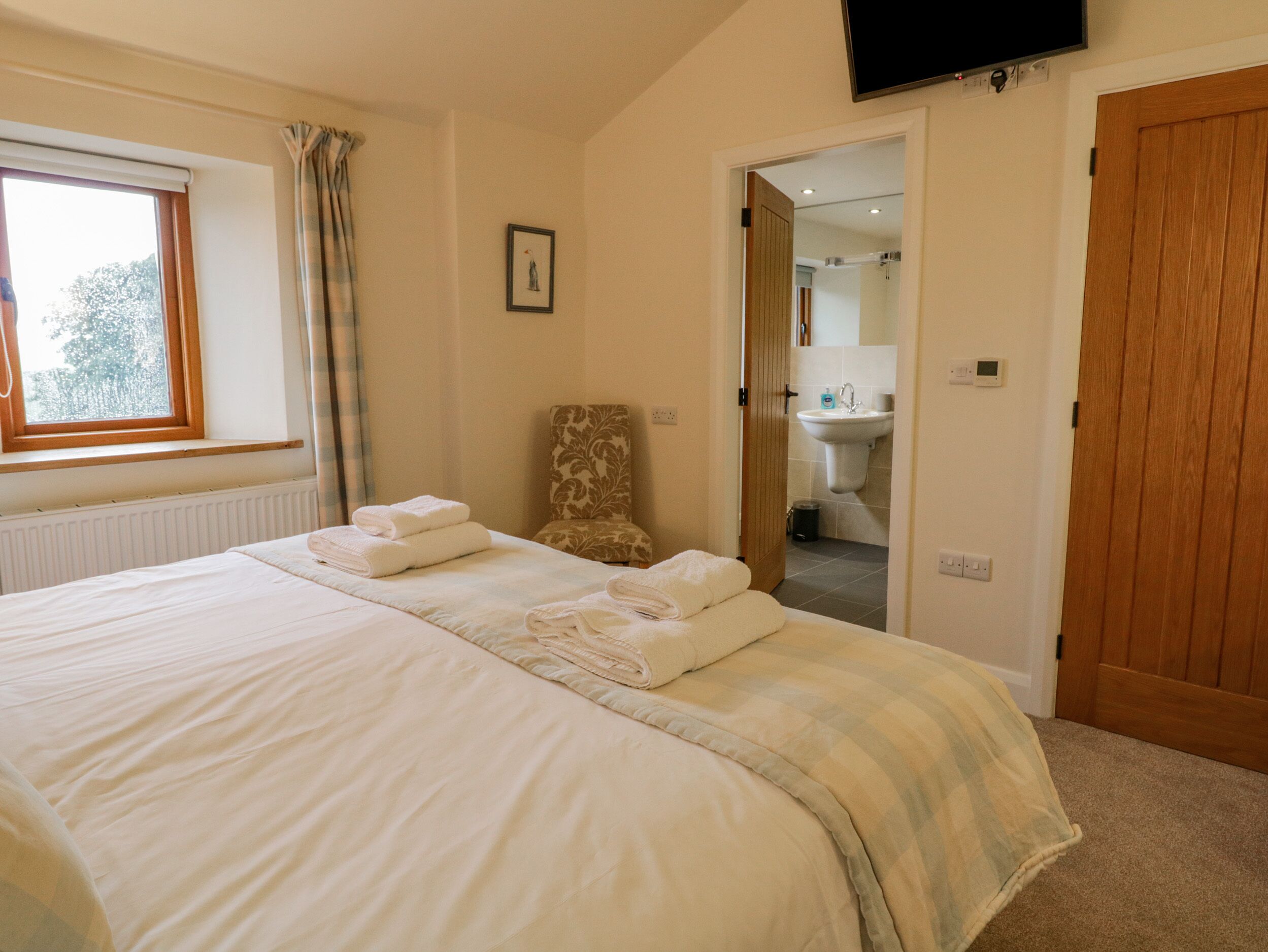 A bedroom with a large bed, a chair, a window, and a TV.