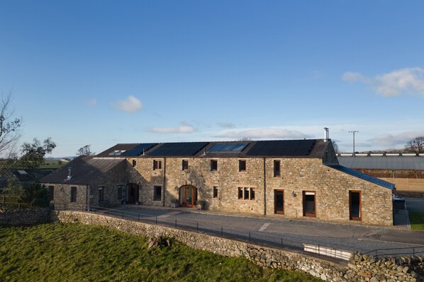 A stone building with multiple windows and a sloped roof, featuring solar panels. - Coppa Hill Barn (Carnforth)
