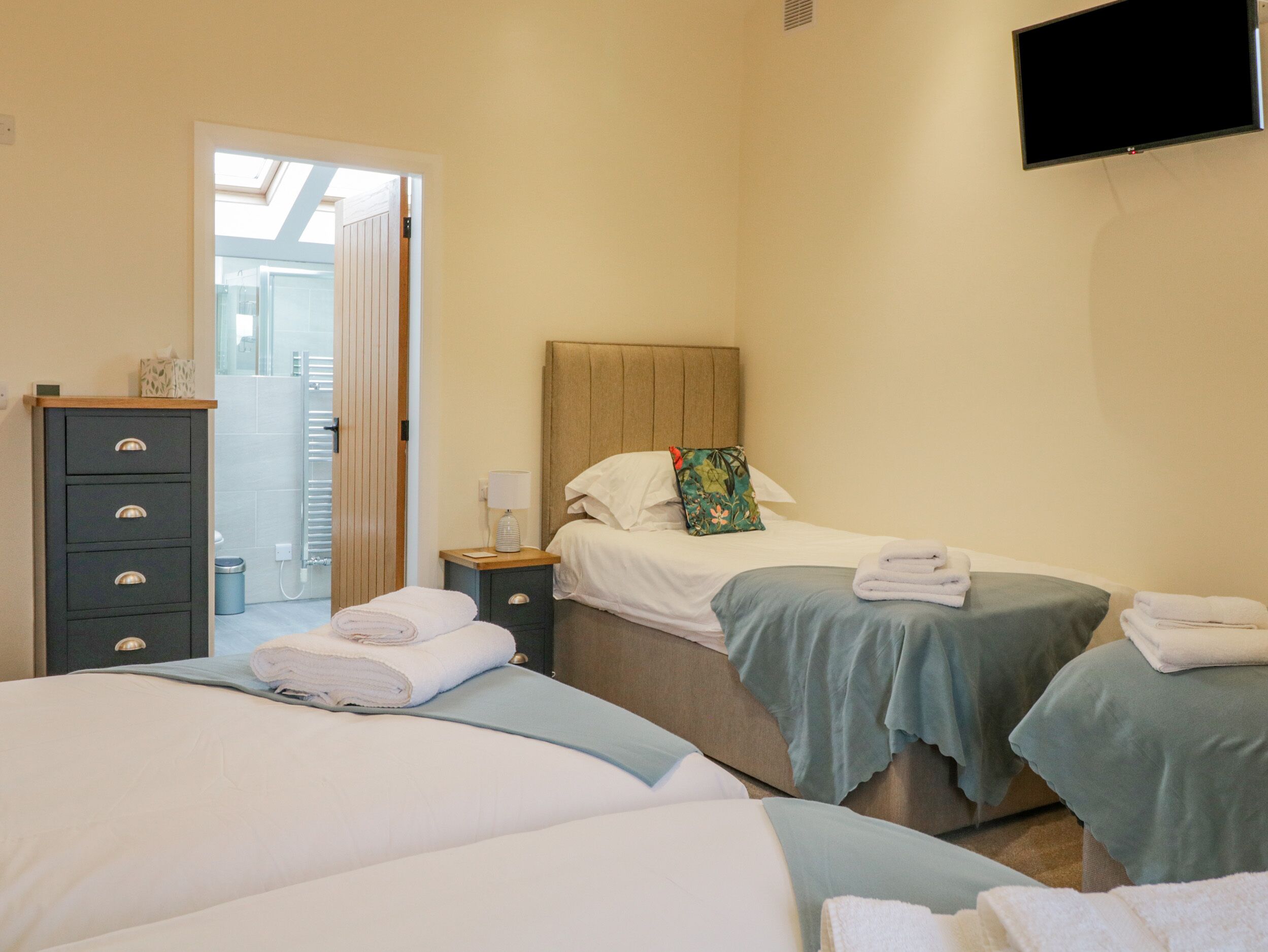 A hotel room with two beds, a nightstand, a dresser, and a TV mounted on the wall.