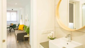 A modern bathroom with a round mirror, a white sink, and a potted orchid. - Deluxe Beach Canteras Flat 3br Wifi Free 1ºA (Palmas De Gran Canaria, Las)