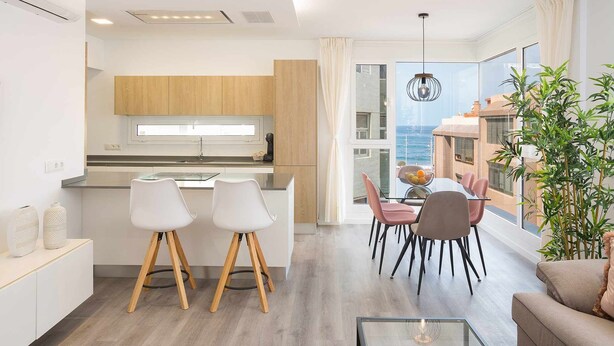 A modern kitchen with wooden cabinets, a dining area with a table and chairs, and a large window overlooking the sea. - Deluxe Beach Canteras Flat 3br Wifi Free 1ºA (Palmas De Gran Canaria, Las)