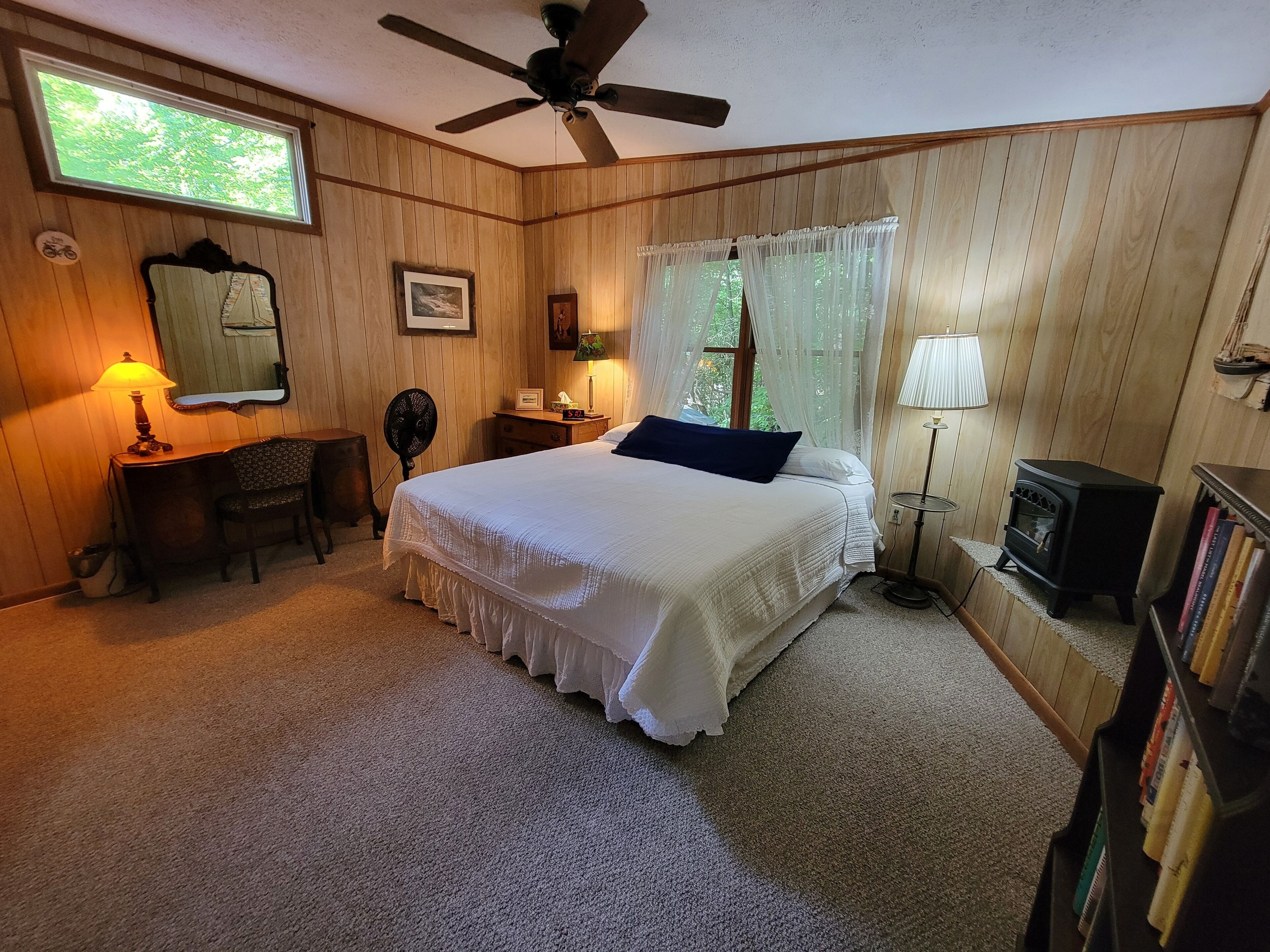 Une chambre à coucher comprenant un lit, un bureau, une chaise, un ventilateur, un radiateur et une bibliothèque.