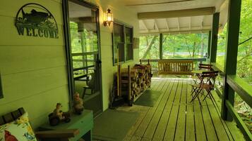 Une véranda en bois avec un banc, une table et une pancarte de bienvenue.
