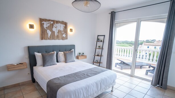 Ein Schlafzimmer mit einem großen Bett, einer Weltkarte als Wandbild, einem Hängeregalsystem und einem Balkon mit Gartenmöbeln.