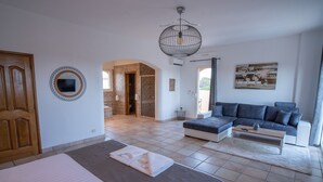 Ein modernes Schlafzimmer mit Bett, Sofa und Couchtisch. Durch einen Bogen ist ein Badezimmer mit Dusche und Toilette zu sehen.