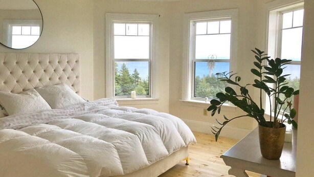 Un dormitorio con cabecera capitonada, una cama grande y vistas al exterior a través de tres ventanas.