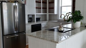 Una cocina moderna con armarios blancos, un refrigerador de acero inoxidable, lavavajillas empotrado, cafetera y hervidor sobre la encimera.