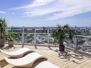A rooftop terrace with lounge chairs, potted plants, and a city view.