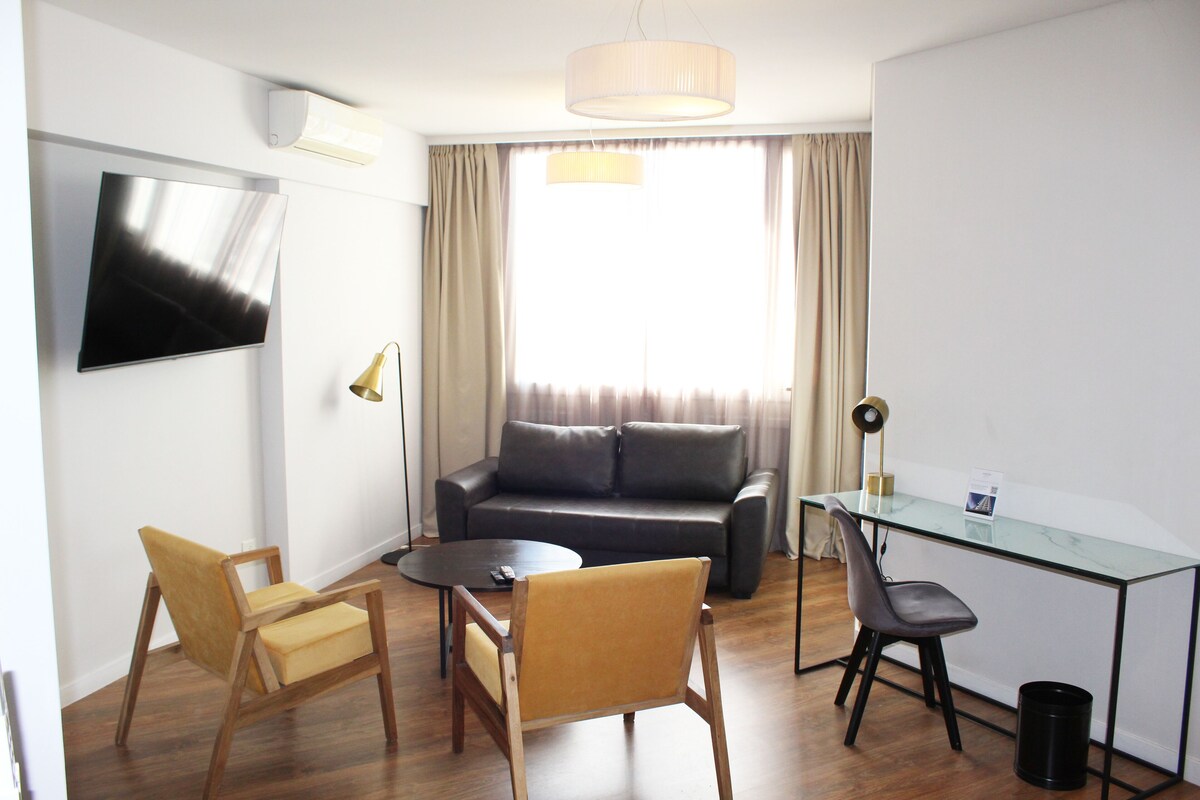 Een moderne woonkamer met een glazen bureau, twee stoelen, een bank en een televisie.