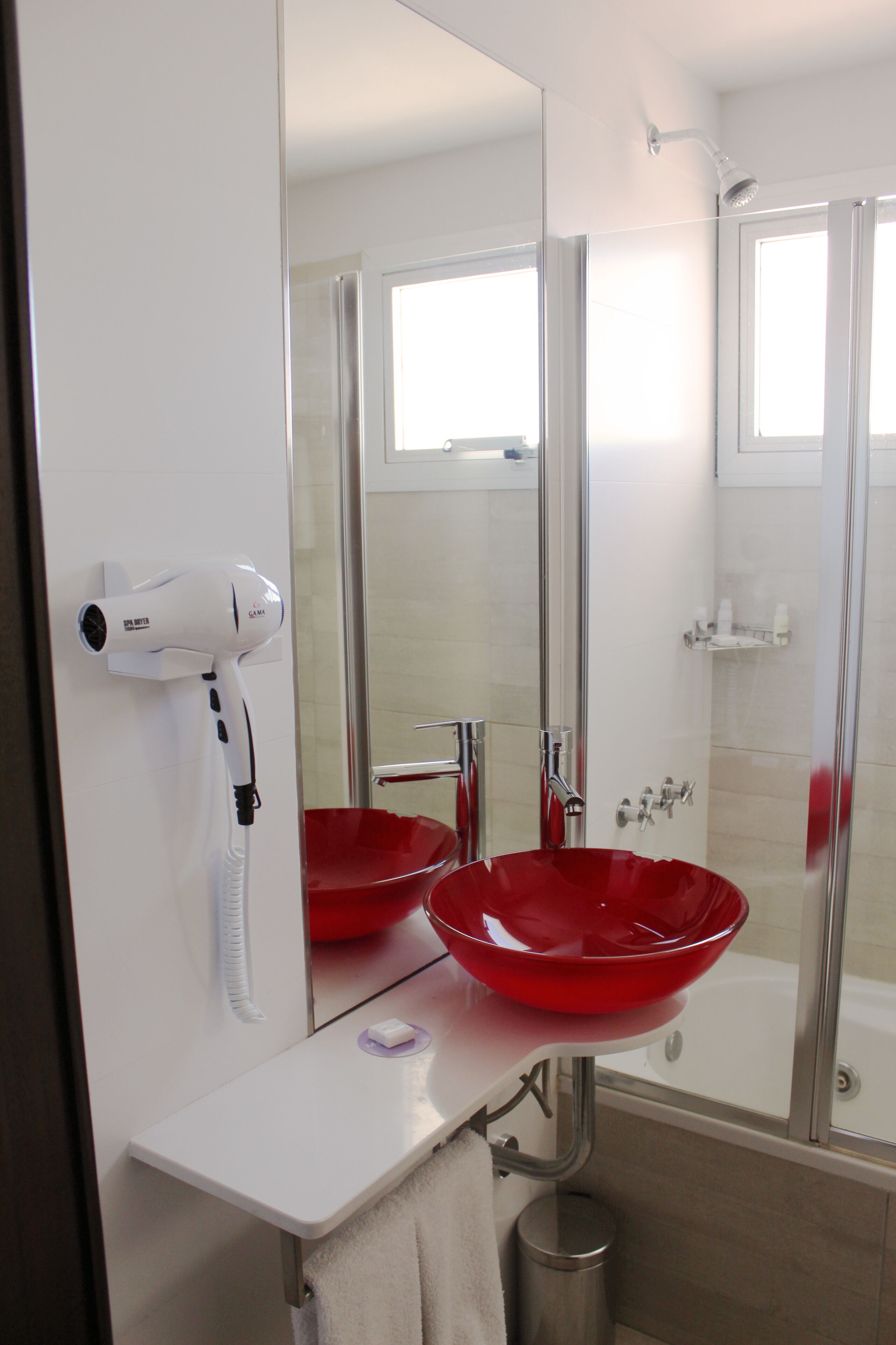 A bathroom with a white sink, red basin, and a hairdryer on the wall.