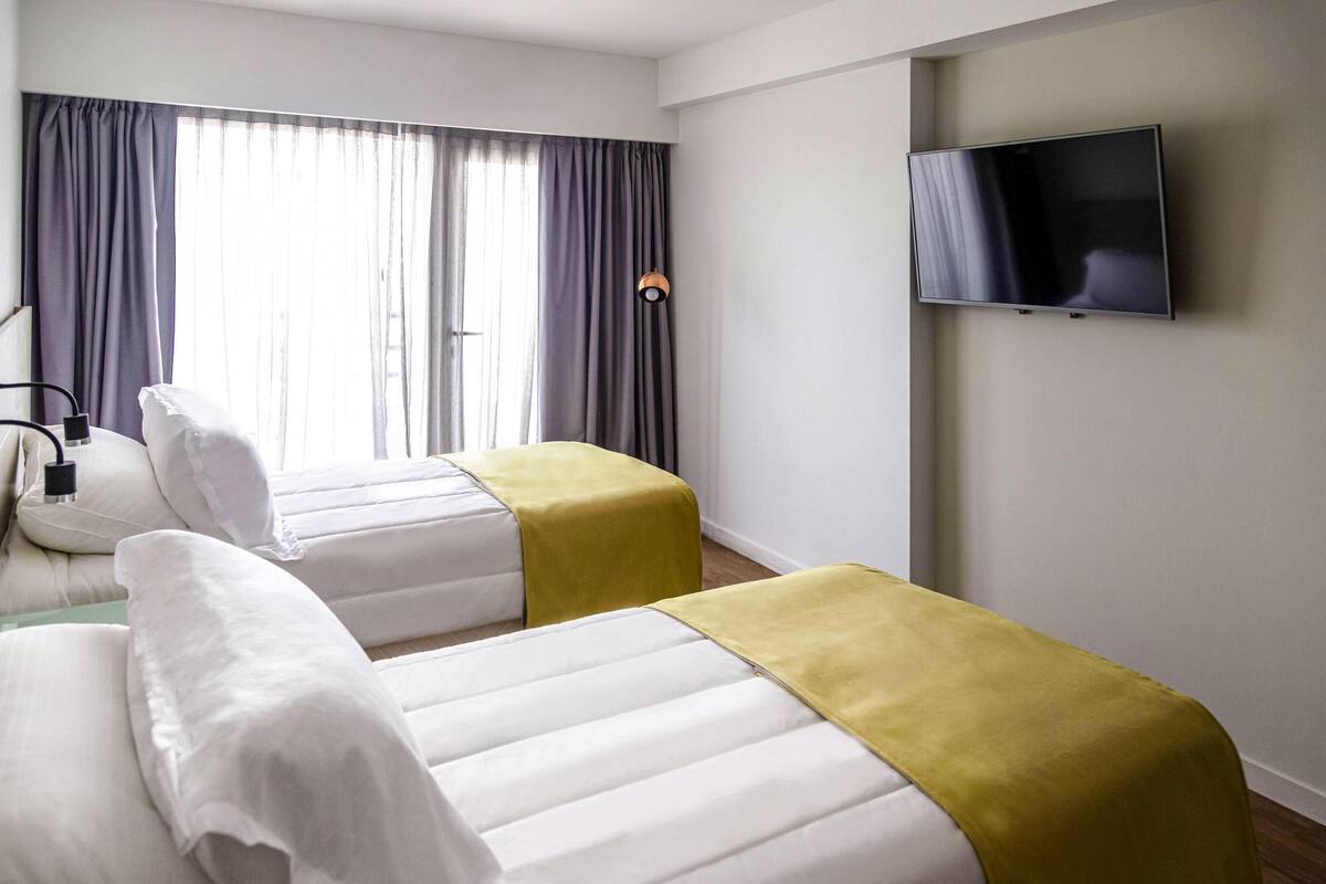 Een hotelkamer met twee bedden, een televisie aan de muur en een raam met gordijnen.