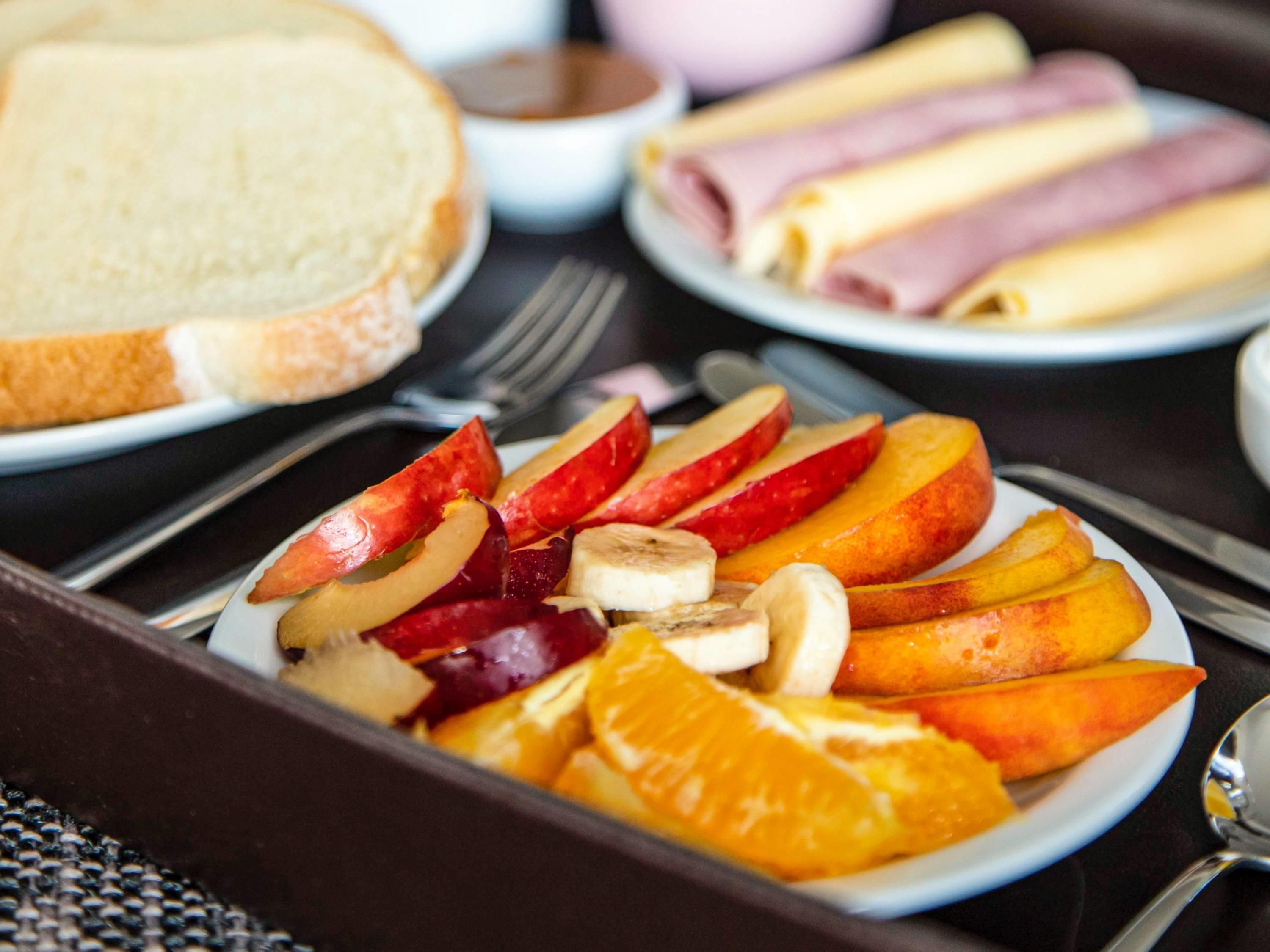 Een ontbijtje met gesneden fruit en een belegd broodje.