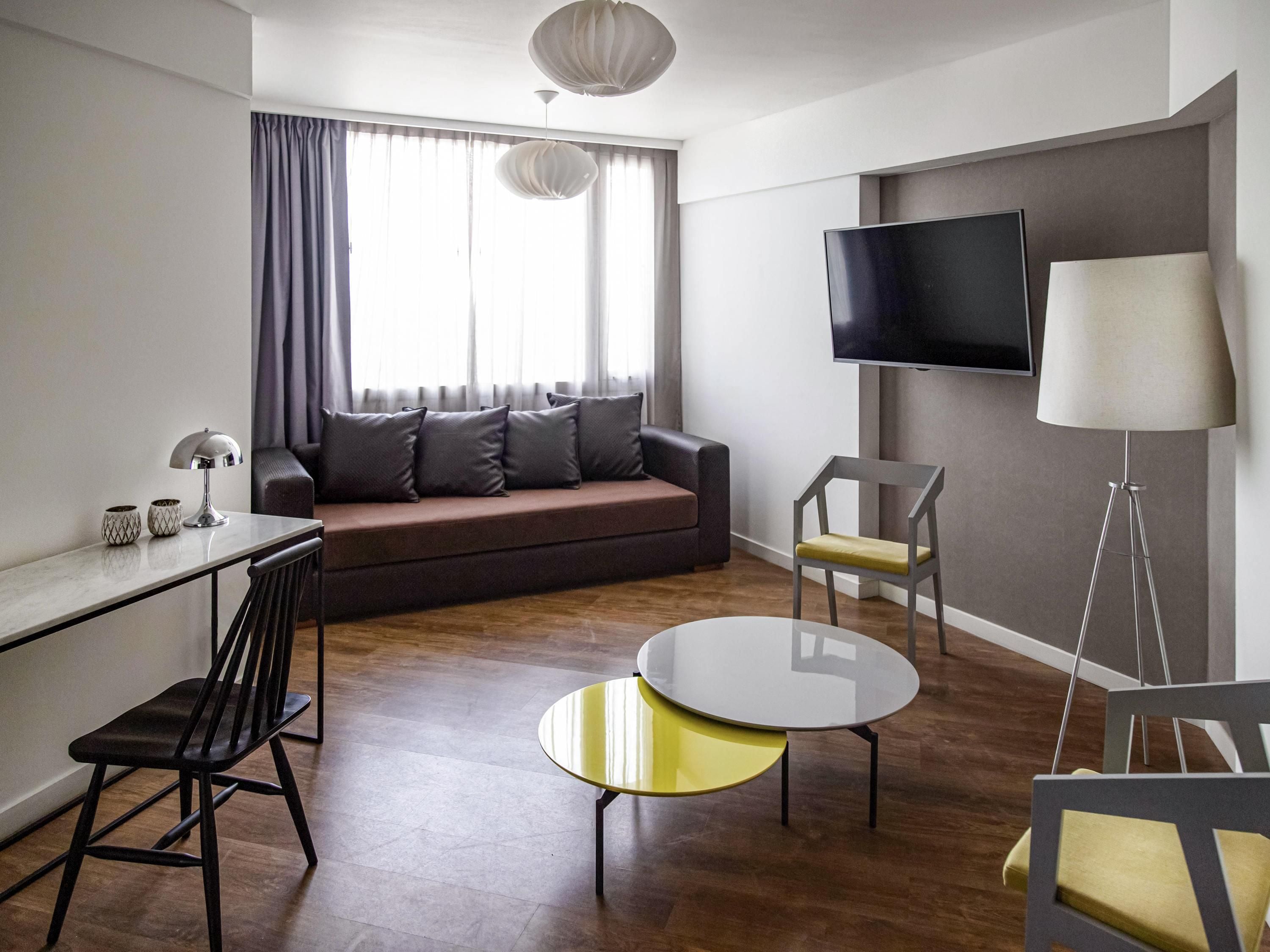 A modern living room with a sofa, a TV mounted on the wall, a dining table, and a floor lamp.