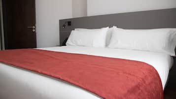 Habitación de hotel con cama, una manta roja, ropa de cama blanca, una puerta de madera y cabecero con interruptor de luz.