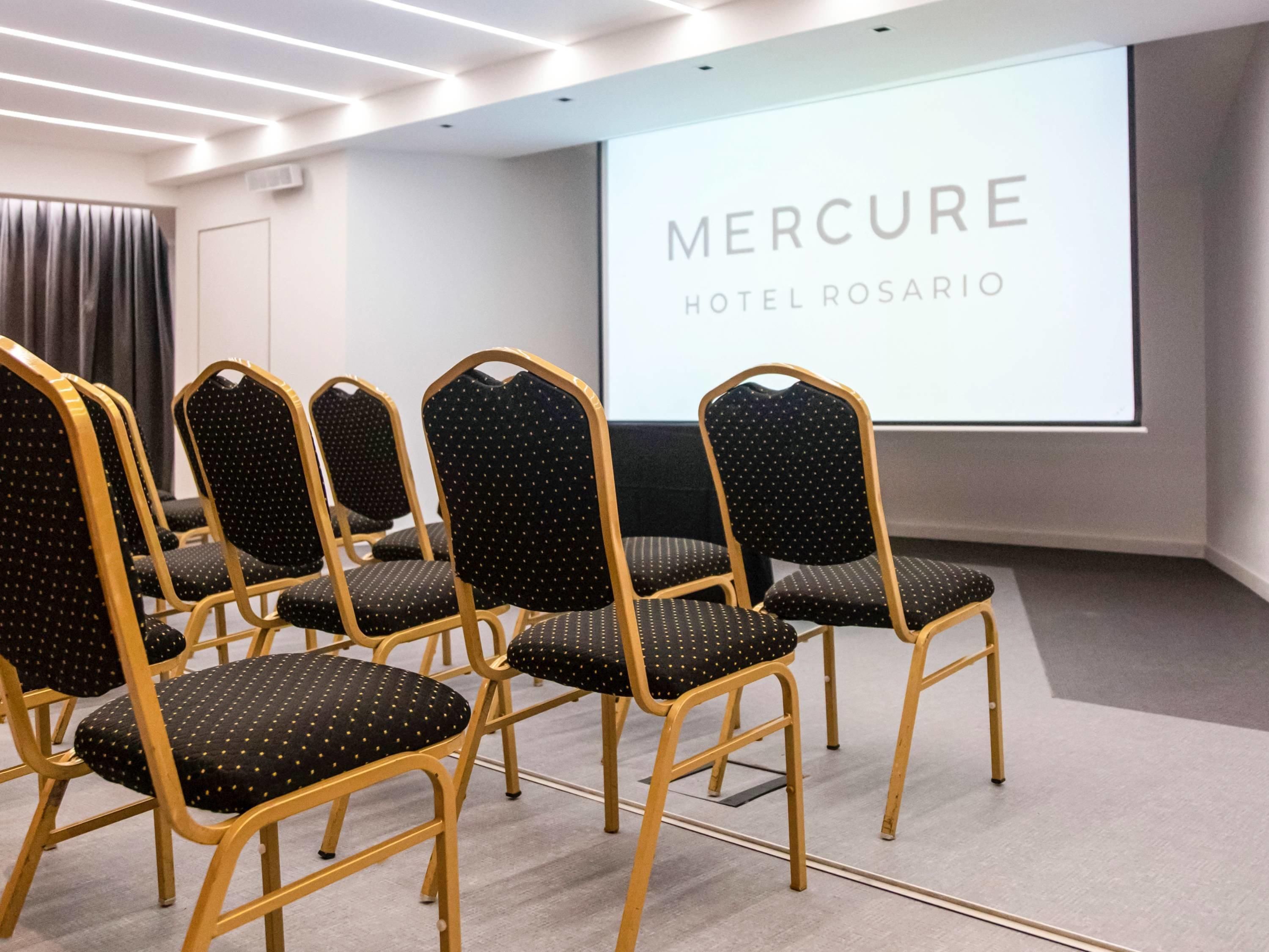A conference room with rows of chairs and a projection screen displaying 'MERCURE HOTEL ROSARIO'.