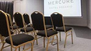 A conference room with rows of chairs, a projection screen displaying "Mercure Hotel Rosario", and modern lighting fixtures.