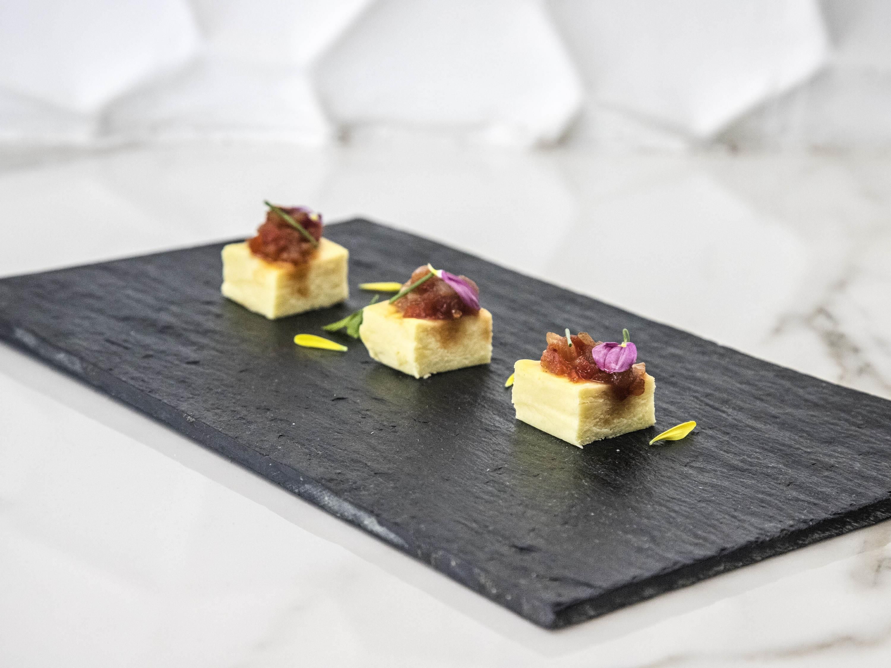 Drei quadratische Desserts auf einer dunklen Schieferplatte.