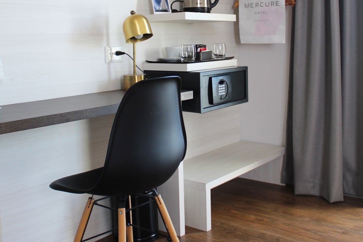 Een moderne hotelkamer met een zwarte stoel, een bureau met een lamp, een minibar en een gordijn.