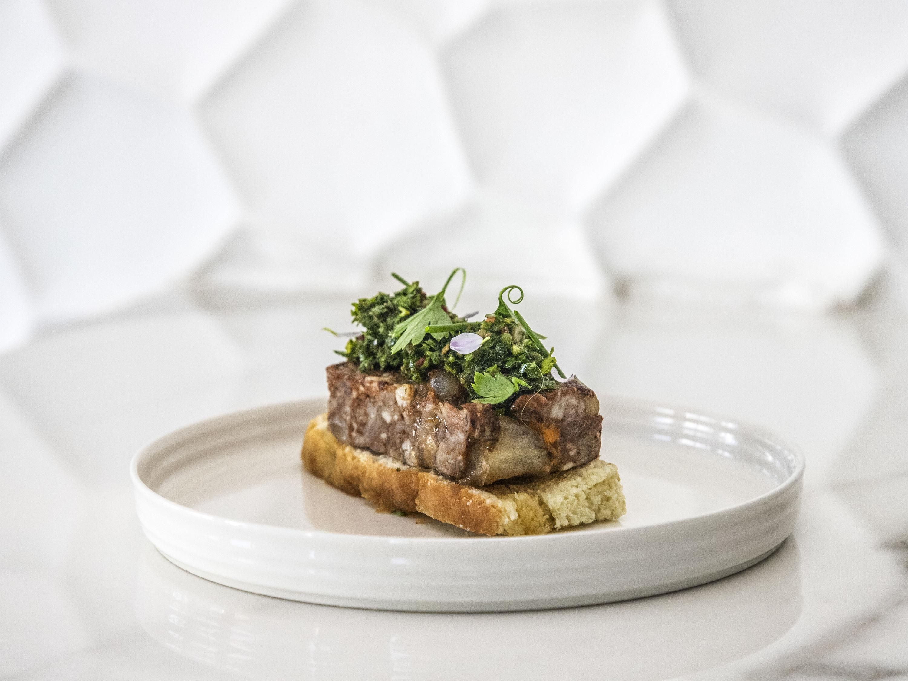 A plate with a meat dish on a slice of bread, garnished with greens, on a white plate.