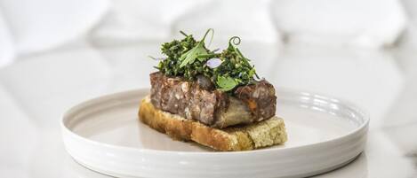 A plate with a meat dish on a slice of bread, garnished with greens, on a white plate.