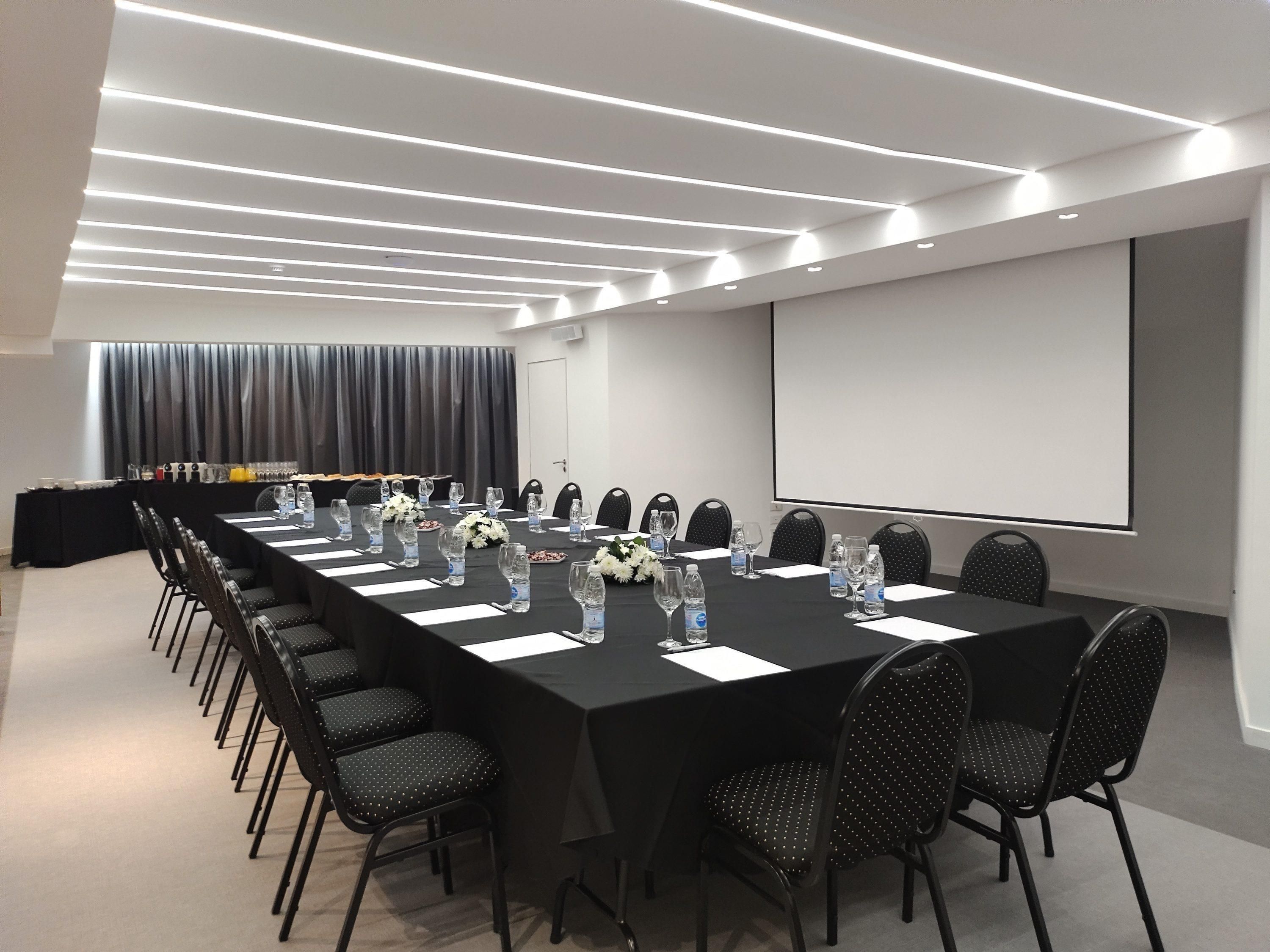 A conference room with a long table, chairs, a projector screen, and a curtain backdrop.