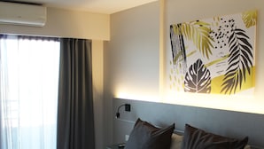 Une chambre d’hôtel moderne avec un grand lit, une table de chevet, un climatiseur fixé au mur et une fenêtre avec des rideaux.