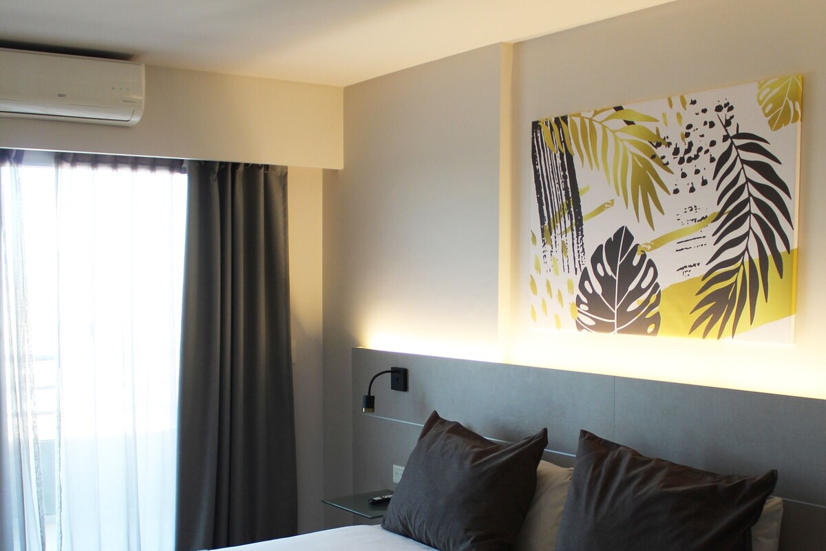 Een moderne hotelkamer met een groot bed, een nachtkastje, een wandairconditioner en een raam met gordijnen.