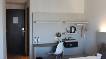 Una habitación de hotel moderna con una cama, un escritorio con silla, una pequeña kitchenette y acceso al baño.