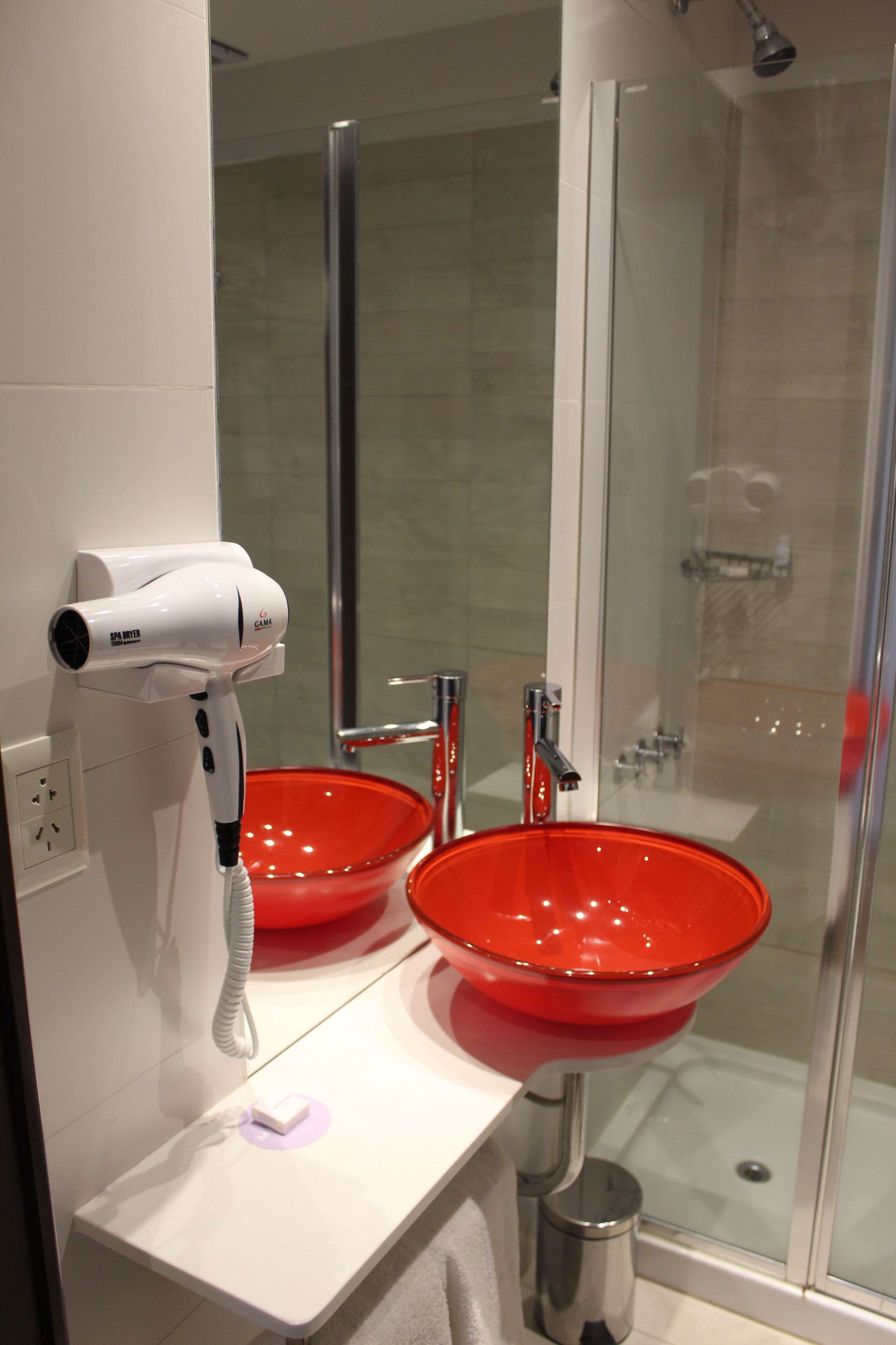 Un baño con lavamanos blanco, lavabo rojo y un secador de pelo sobre el mostrador.