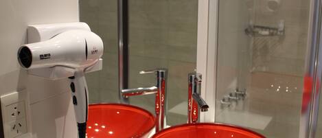 Un baño con lavamanos blanco, lavabo rojo y un secador de pelo sobre el mostrador.