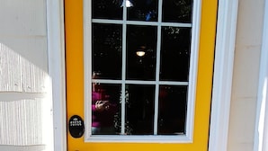 Una puerta amarilla con una ventana, un timbre y un tapete colorido sobre un piso de madera.
