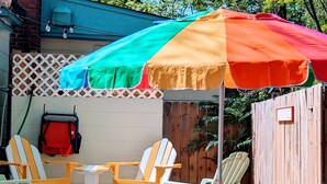 Un patio con una mesa de madera y dos sillas, un paraguas colorido y una cerca de madera.