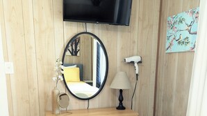 Una habitación con pared de madera, un televisor de pantalla plana sobre un escritorio, un espejo, una lámpara y una silla.
