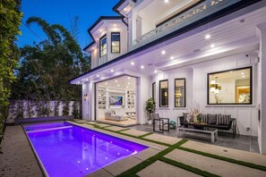A modern house with a large outdoor pool, a patio area, and a well-lit interior. - Gardner Modern - Exquisite Modern Villa with Pool & Theater in Beverly Grove (Los Angeles)