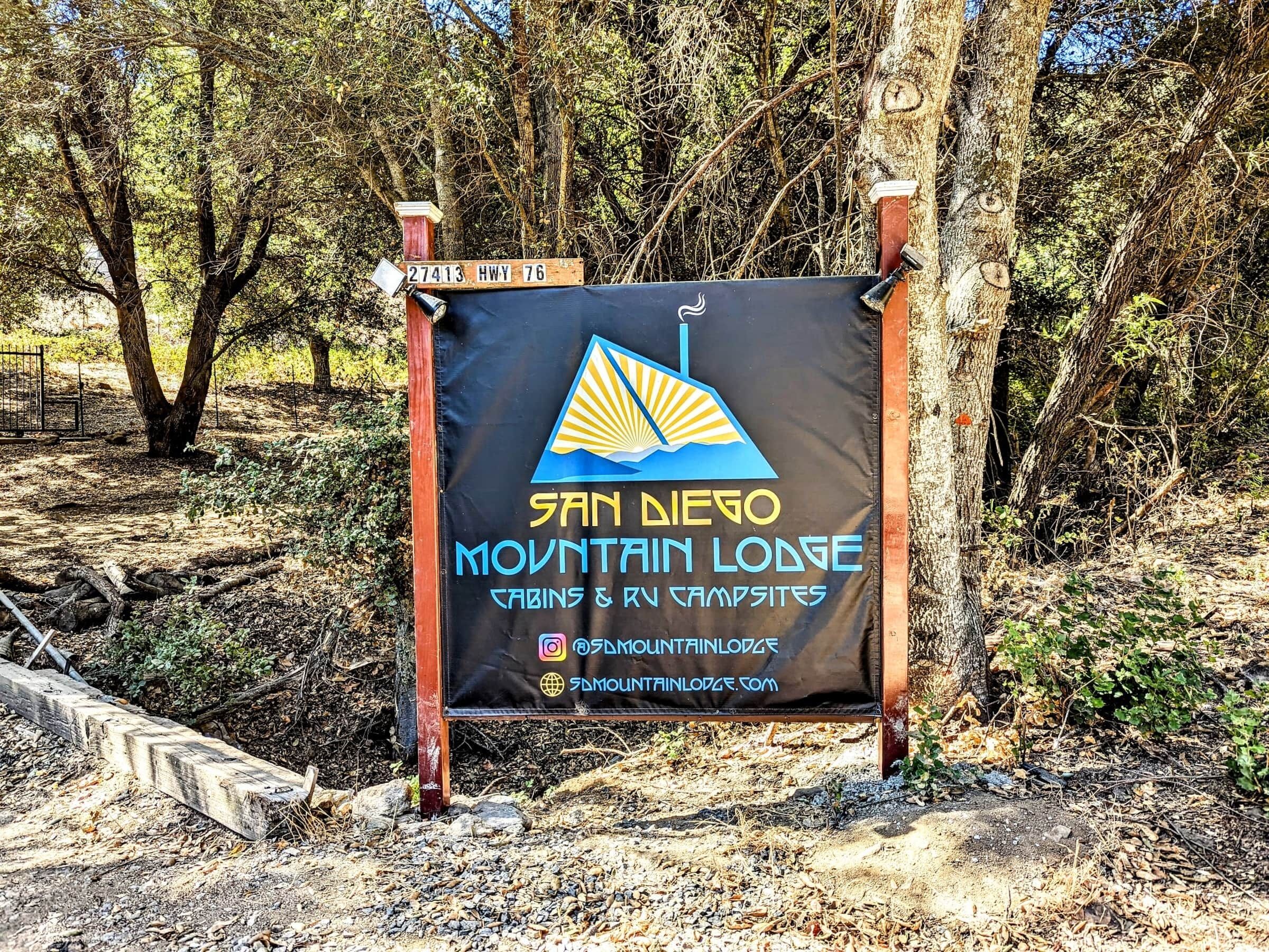 Une enseigne pour le San Diego Mountain Lodge, avec un logo, le nom de l’établissement et les liens vers ses réseaux sociaux.