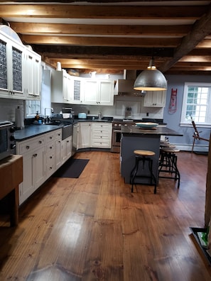 Une cuisine avec un plancher en bois, des armoires blanches, un îlot central doté de tabourets et un luminaire suspendu.
