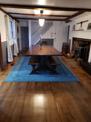 Une table à manger en bois avec des bancs, un tapis bleu, un escalier et une cheminée.