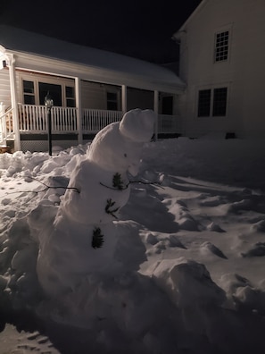 Un bonhomme de neige dans une cour enneigée, avec une maison en arrière-plan.