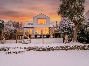 Una casa de dos pisos con un balcón, rodeada de árboles cubiertos de nieve y un cielo despejado.